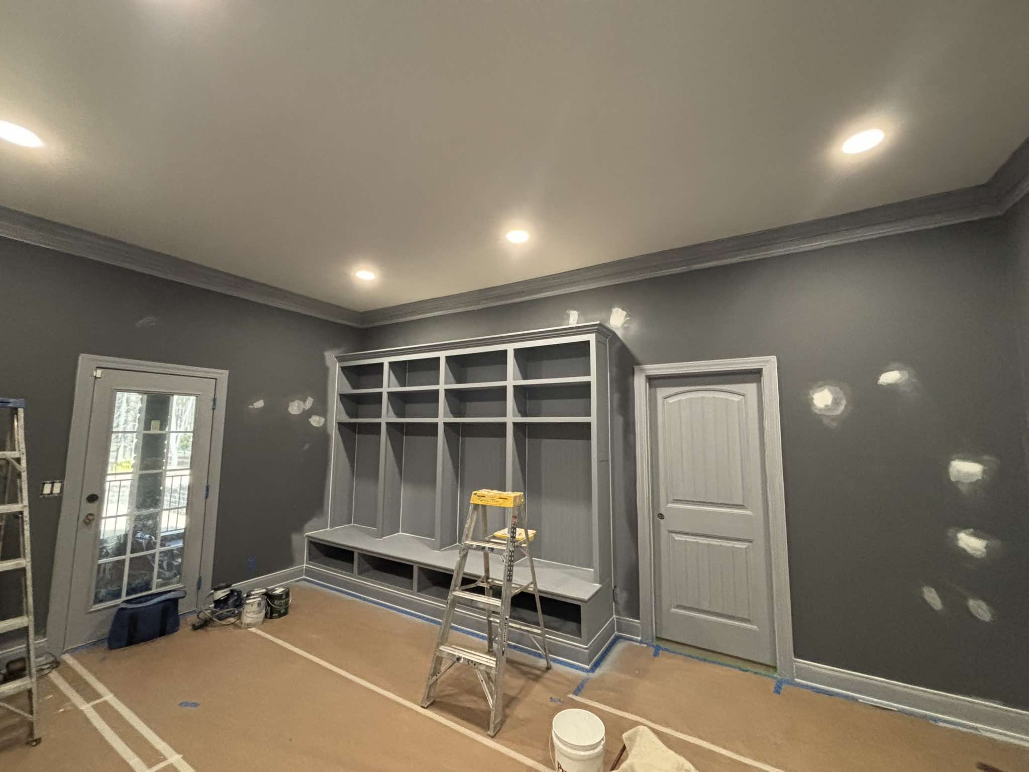 Interior wall preparation with visible patches beside gray built-ins and a protected floor