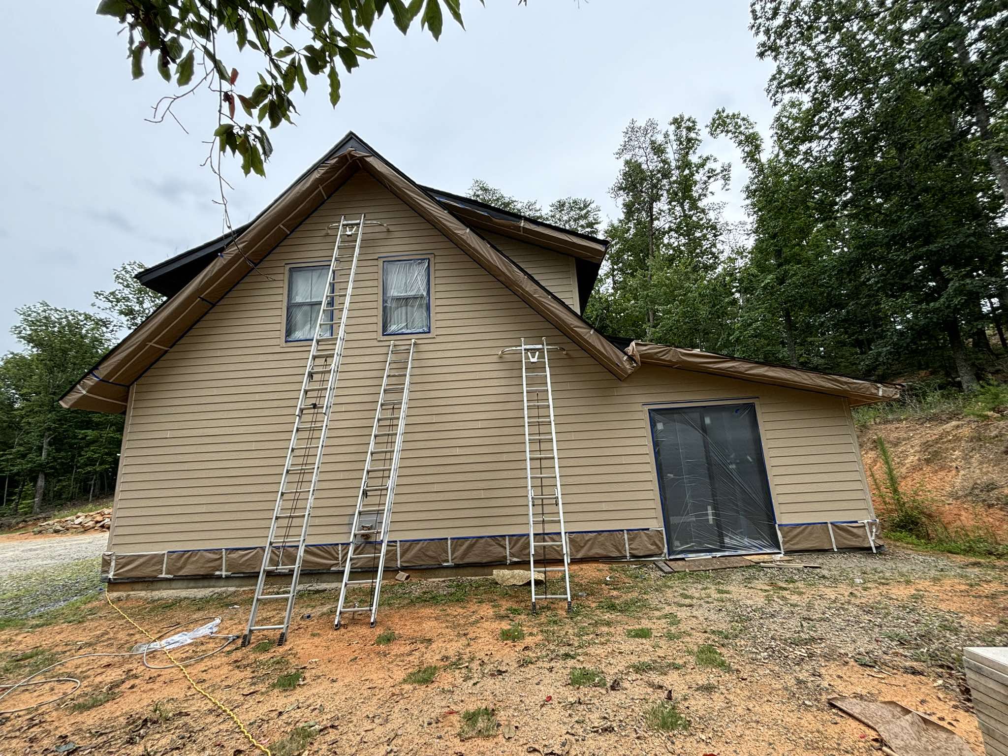Rear garage elevation before painting with tan siding and ladders positioned along the wall