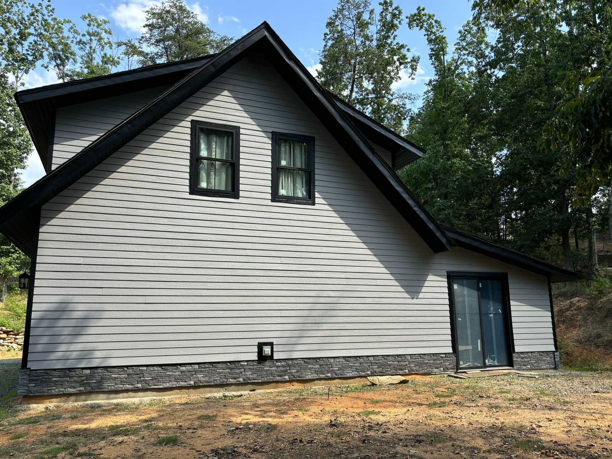 Finished side elevation showing light gray siding, black windows, dark trim, and a stone base