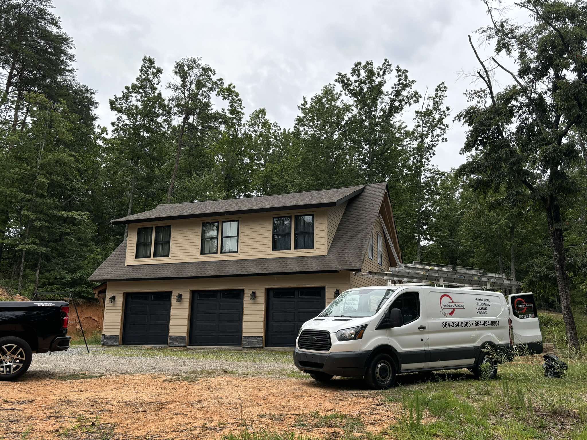 Front of the three-car garage before painting with tan siding, dark doors, and a work van nearby