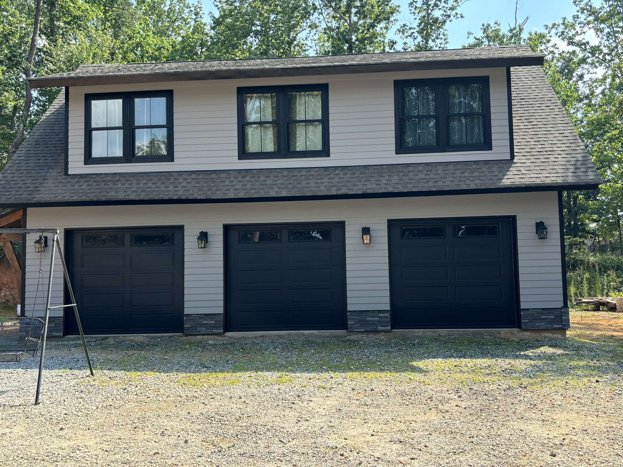 Straight-on finished view of three dark garage doors beneath light gray siding and black trim