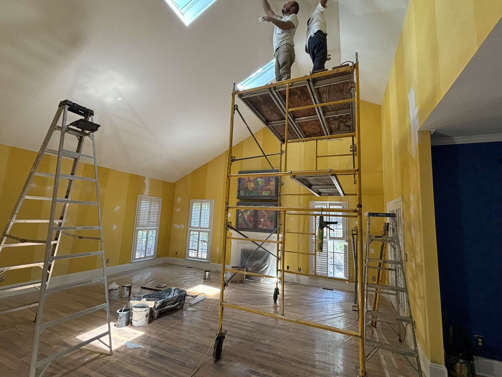 Painter working from scaffold near the skylights in the tall yellow interior