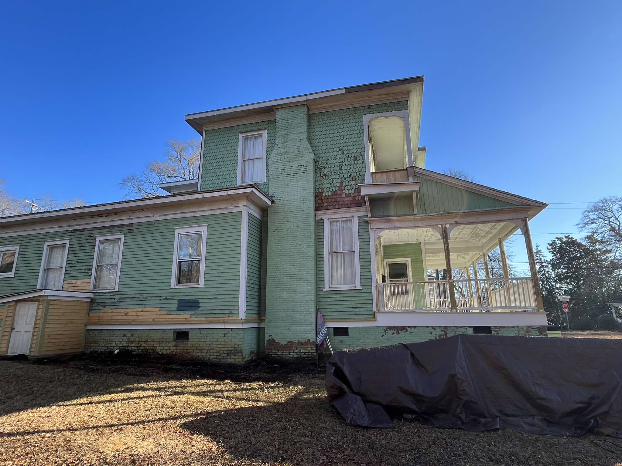 Rear addition during exterior work with light green siding and the ground protected below