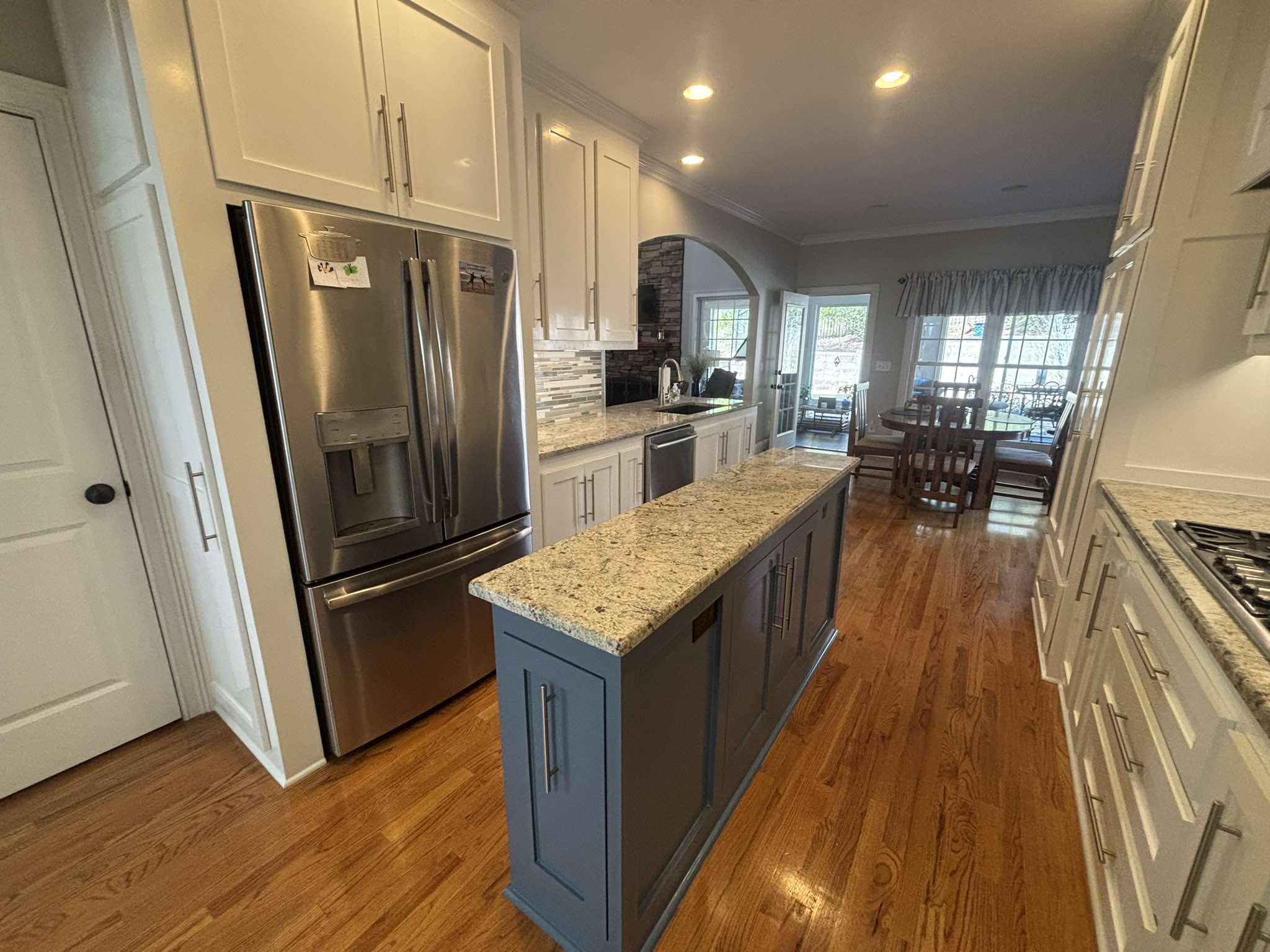 Finished galley view with white cabinets, a dark island, granite counters, and a stainless refrigerator