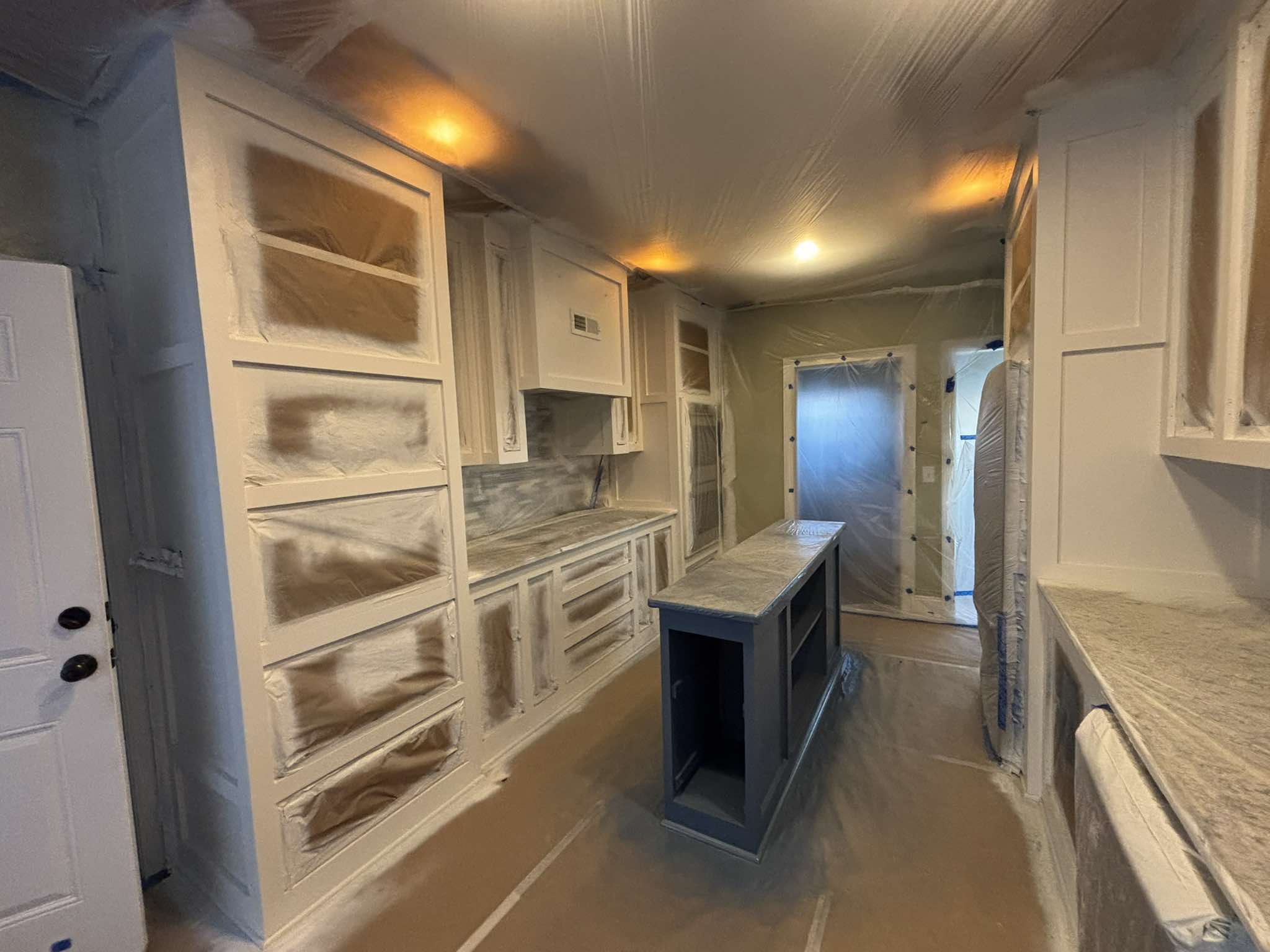 Protected kitchen cabinets and island viewed from the doorway during the painting process