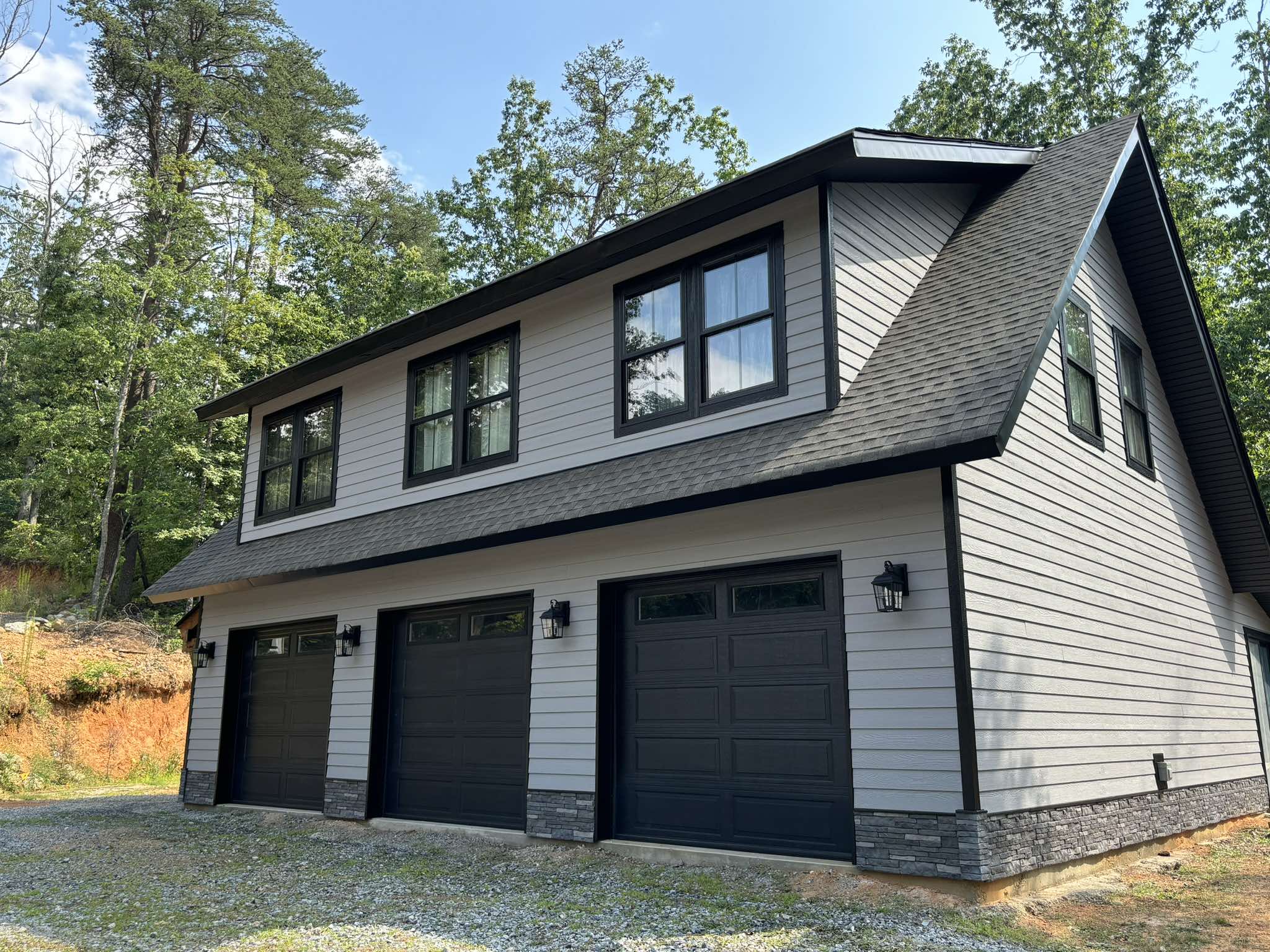 Freshly painted garage with light gray siding, black trim, and three dark garage doors